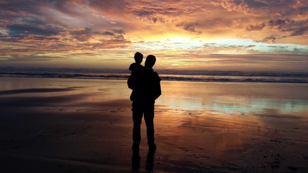 Vater mit Kind dem Arm am Strand.